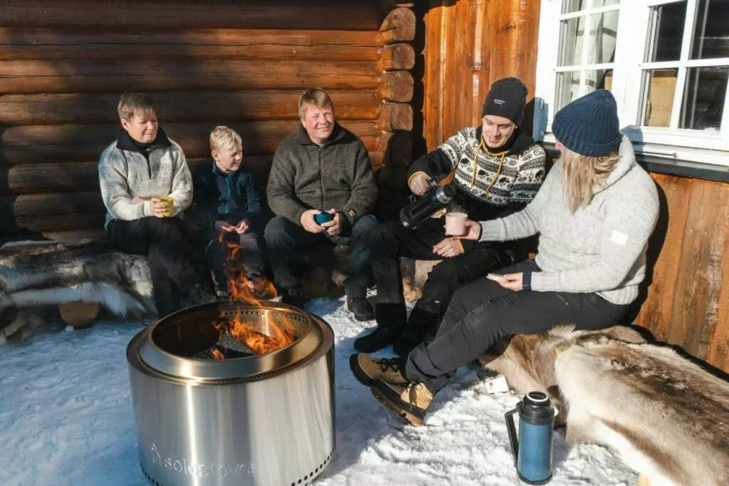 Familie rundt et bål foran en tømmervegg – fotografering for Bålstedet
