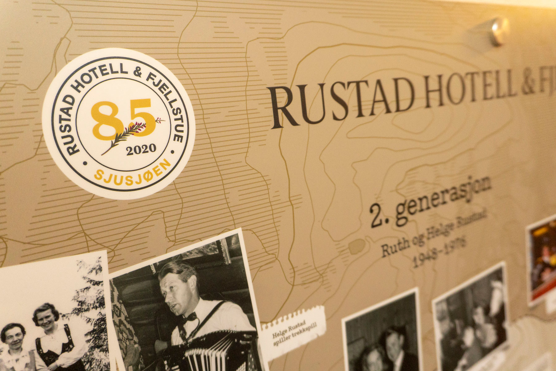 Jubileumslogo for 85 års drift på fotoveggen til Rustad Hotell og Fjellstue