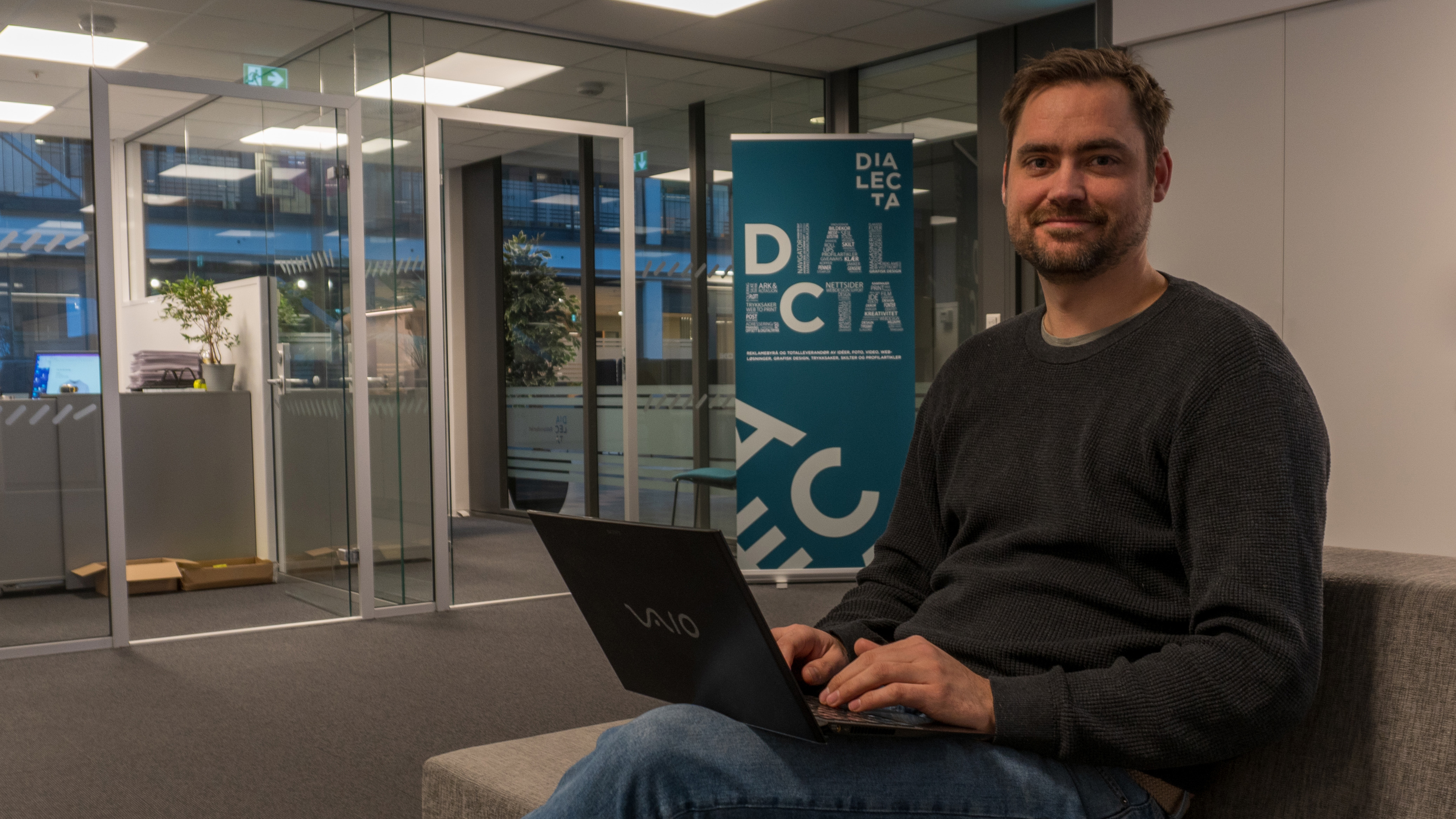 Mann med bærbar PC foran en Dialecta-rollup i et kontorlokale