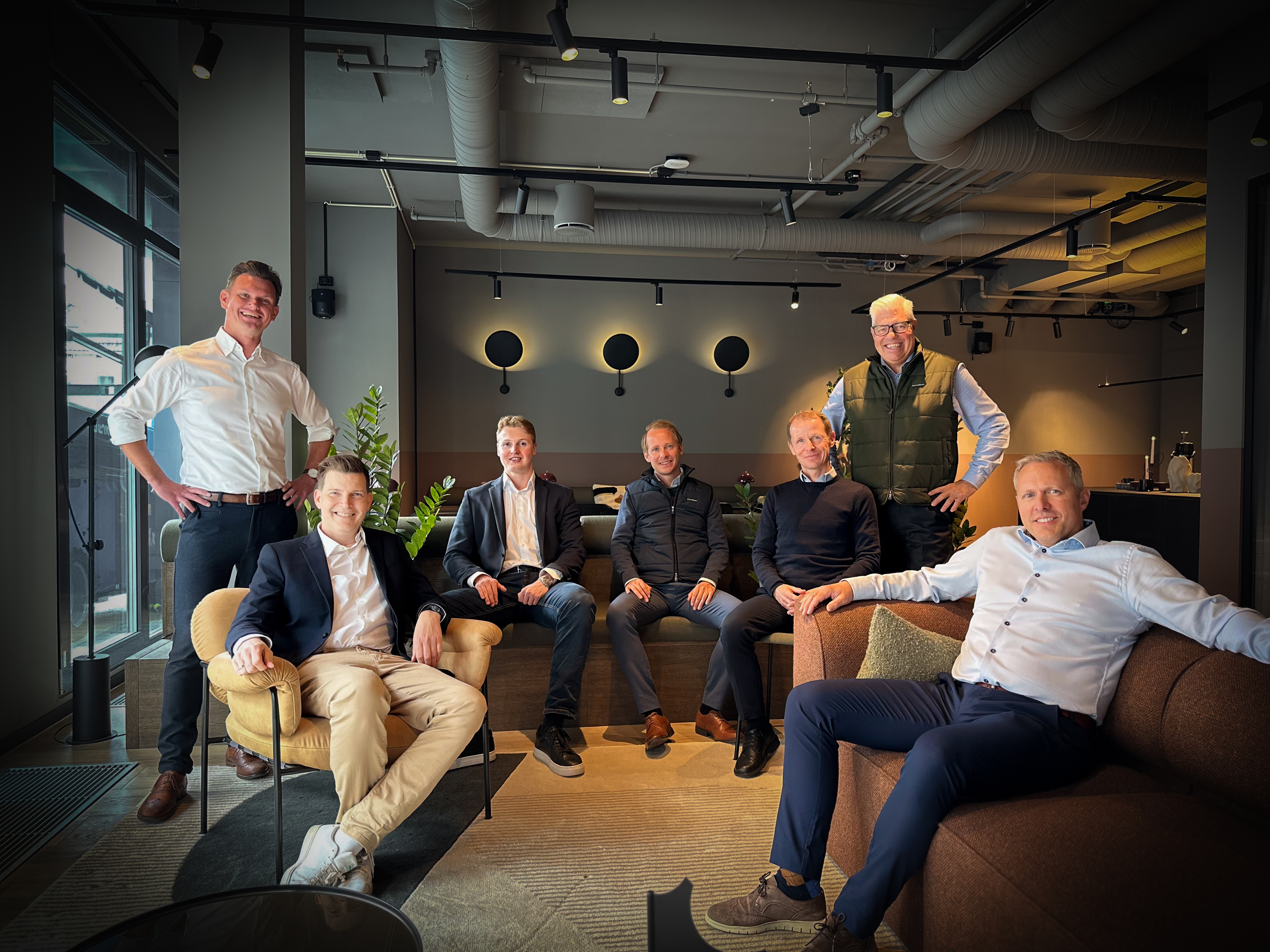 Sju menn samlet i en sofagruppe i et moderne loungelokale