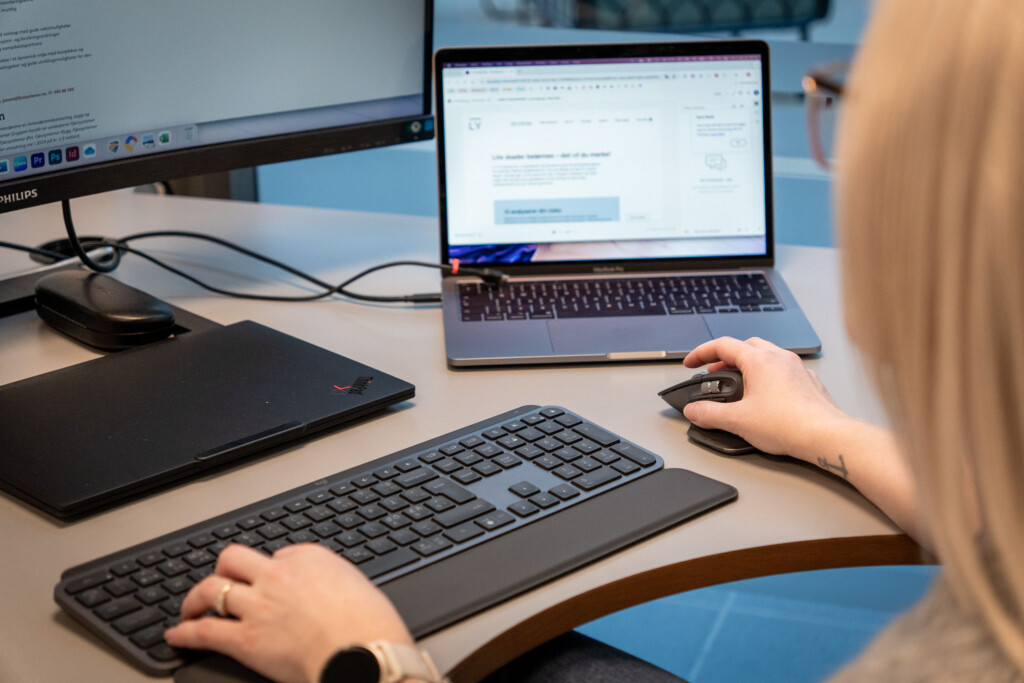 Person jobber på tastatur foran en bærbar PC og en ekstra skjerm